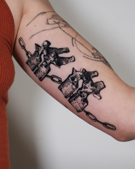 Wirbelkörper und Ketten Tattoo am Oberarm Innen